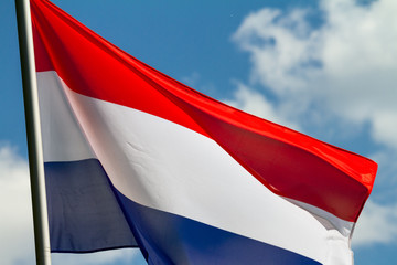 Wall Mural - Flag of the Netherlands waving in the wind on flagpole against the sky with clouds on sunny day, close-up