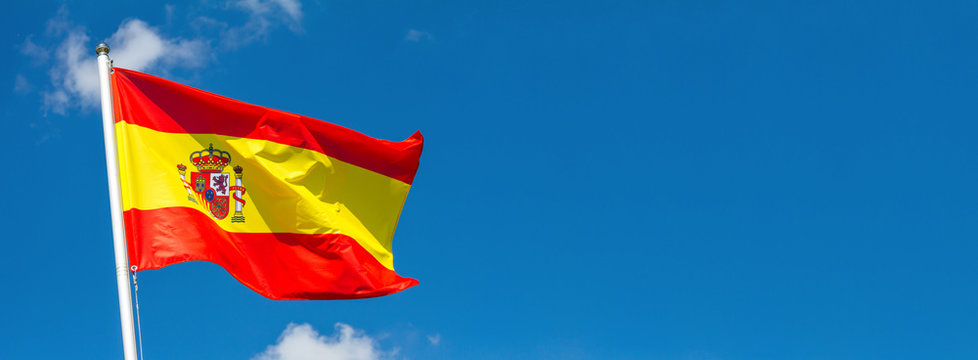 flag of spain waving in the wind on flagpole against the sky with clouds on sunny day, banner, close