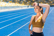 © LIGHTFIELD STUDIOS - athletic female jogger wiping sweat after run on track at sports stadium