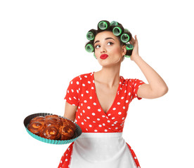 Poster - Funny young housewife with hair rollers holding homemade pastry on white background