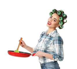 Poster - Funny young housewife with hair rollers holding spoon and frying pan on white background