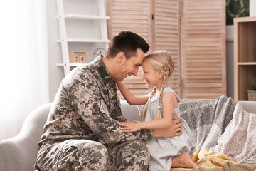 Young man in military uniform with his little daughter on sofa at home