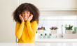 © Krakenimages.com - African american woman wearing yellow sweater at kitchen covering ears with fingers with annoyed expression for the noise of loud music. Deaf concept.
