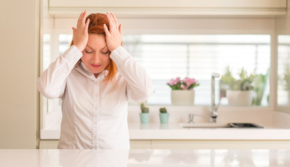 Poster - Redhead woman at kitchen suffering from headache desperate and stressed because pain and migraine. Hands on head.