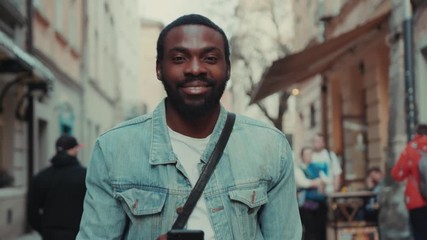 Portrait young african amerian man goes down the street and uses phone look at camers happy smile internet face technology fashion black texting attractive smartphone communication handsome message