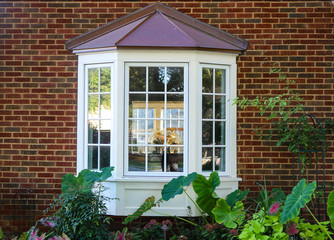 Wall Mural - Bay window in a brick house with reflection of trees and view of windows and flowers inside and flowers and elephant ears outside