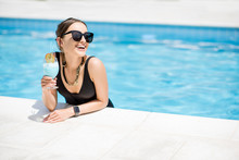 Portrait Of A Beautiful Woman In Black Swimsuit Relaxing With Cocktail At The Swimming Pool Outdoors