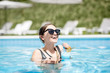 © rh2010 - Beautiful woman in black swimsuit and sunglasses swimming with cocktail in the water pool outdoors