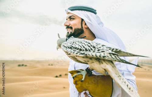 Obraz Dibond Arabski mężczyzna z tradycyjnymi emiratami ubrania idący na pustyni ze swoim ptakiem sokoła