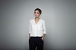 Interested businesswoman with trendy makeup posing on gray background in studio. Indoor photo of serious young lady in white blouses classic black pants standing in confident pose.