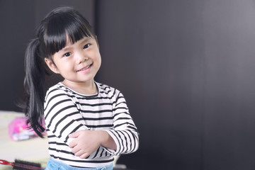 Wall Mural - Asian children cute or kid girl feel business child with cross one's arm and smile white teeth with confidence after dressed up in the room at home office on black with space