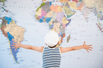 little child in captain hat spreading hands to world map before travel