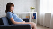 © Di Studio - thoughtful pregnant woman sitting on sofa in living room