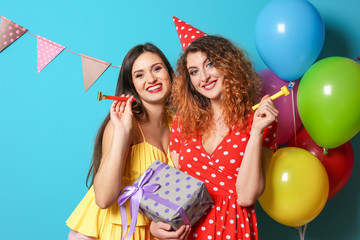 Wall Mural - Young women with party blowers and gift box on color background. Birthday celebration