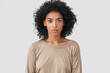 Indoor shot of serious dark skinned female freelancer has Afro hairstyle, pleasant appearance, dressed in beige casual sweater, works distantly at home, enjoys domestic atmosphere. Ethnicity concept