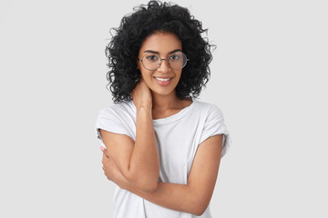 Wall Mural - Horizontal shot of shy young mixed race woman with dark skin, curly hair, looks positively, keeps hand on neck and half crossed, happy to recieve help from handsome man, isolated over white background