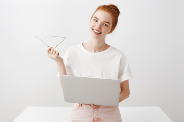 Wall Mural - Guy asking coworker for coffee. Attractive friendly female with ginger hair and beautiful clean skin taking off glasses, tilting head, gazing at camera, holding laptop on lap, doing homework in app