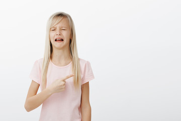 but i want that toy mom. portrait of whining disobedient little girl in pink t-shirt, pointing right