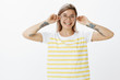 © Cookie Studio - Birthday girl pulling ears up for each year she was born. Positive good-looking woman in cute yellow striped t-shirt and round glasses, smiling and gazing at camera with pleased playful expression