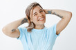 © Cookie Studio - My braces are awesome. Portrait of cute confident and happy young woman in trendy t-shirt, holding hands on back of hear, winking and sticking out tongue playfully, being in great mood over gray wall
