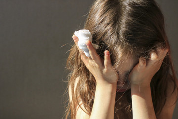 a girl with a bandaged finger cries, covering her face with her hands