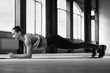 Blacl and white photo of woman with strong body making plank on spacy hall's floor with panoramic windows. looks fit and stunning. Beatiful face, powerful muscles. Wearing stylish sportswear.
