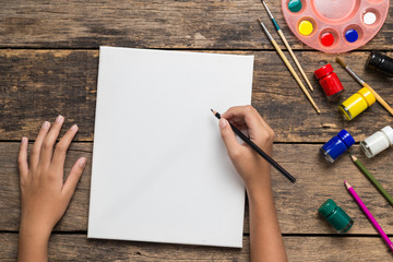 Top view of Girl hand drawing empty paper and colorful pencils, child painting using watercolors and paint brush on old wooden table