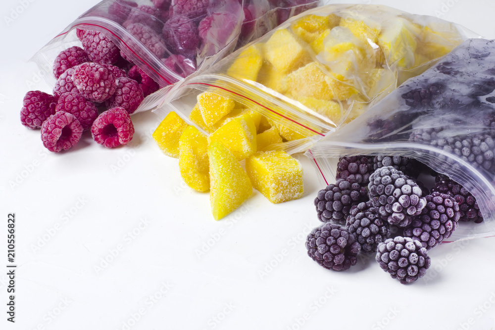 Frozen berries in reusable plastic bags: raspberry, mango and blackberry. White background - obrazy, fototapety, plakaty 