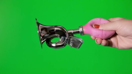 a female hand showing and squeezing a clown's horn. green background.