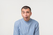 Shocked face of caucasian young man in blue shirt on grey background