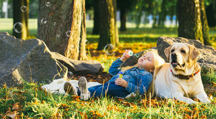 Cute little blonde girl sitting with dog on the grass in the forest