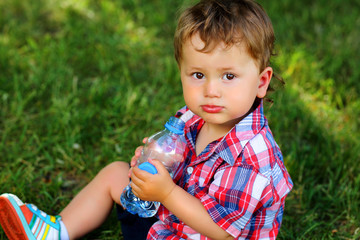 Portrait of a charming boy 1.5 years old in the summer in nature with a bottle of water.