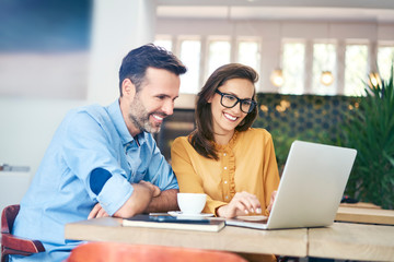 Wall Mural - Joyful couple using laptop while having coffee in cafe together