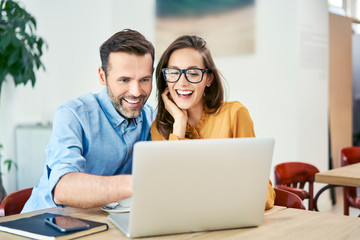 portrait of cheerful couple using laptop together while sitting in cafe