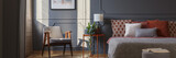 Fototapeta  - Grey armchair standing in dark grey bedroom interior with molding on the wall, orange beside table with plant and lamp and double bed with pillows