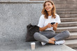 © Drobot Dean - Image of beautiful stylish woman sitting on street stairs with legs crossed on summer day, and holding mobile phone