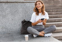 Image Of Beautiful Stylish Woman Sitting On Street Stairs With Legs Crossed On Summer Day, And Holding Mobile Phone