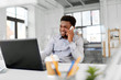 © Syda Productions - business, people, communication and technology concept - smiling african american businessman with laptop computer calling on smartphone at office