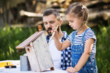 Father With A Small Daughter Outside, Painting Wooden Birdhouse.