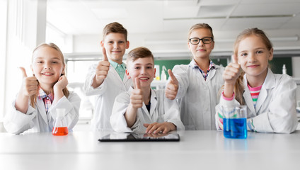 Wall Mural - education, science and technology concept - happy kids with tablet pc computer and test tubes studying chemistry at school laboratory and showing thumbs up