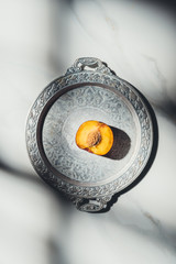 Canvas Print - top view of piece of peach on metal tray on light marble tabletop with shadows