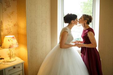 Side view of mother while kissing her daughter and holding her hands at her wedding day. At home.