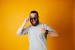 © Vulp - Hot young bearded cheerful man holding sunglasses, laughing at the camera and showing thumb up. Hot offer, summer days.