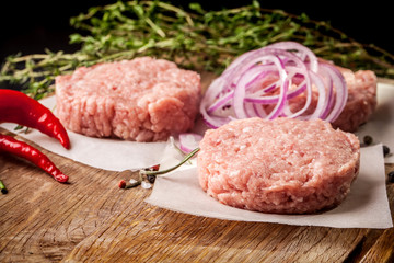 Cutlets from raw minced pork, lamb, veal or beef on parchment. Nearby spices and vegetables. On a black and wooden background. Copy space