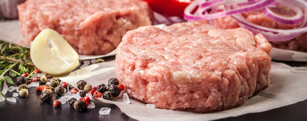 Wall Mural - Cutlets from raw minced pork, lamb, veal or beef on parchment. Nearby spices and vegetables. On a black and wooden background. Copy space