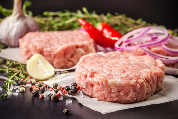 Wall Mural - Cutlets from raw minced pork, lamb, veal or beef on parchment. Nearby spices and vegetables. On a black and wooden background. Copy space