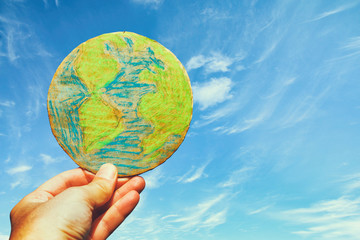 man hand holding earth globe in front of outdoor blue sky background.