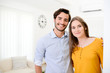 © W PRODUCTION - cheerful young couple man and woman welcome friends at open front door new student home apartment
