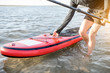 Man carrying red paddleboard on the water, close-up view without face