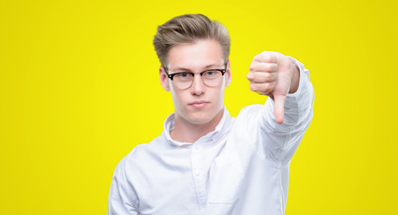 Poster - Young handsome blond man looking unhappy and angry showing rejection and negative with thumbs down gesture. Bad expression.